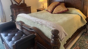 Ein traditionell eingerichtetes Schlafzimmer mit Himmelbett, einem Holzstuhl, einem Nachttisch mit Lampe und einem Spiegel.