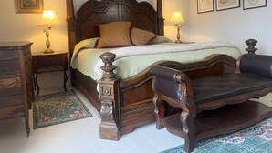 Ein Bett mit Baldachin, verziert mit aufwendigen Holzschnitzereien, zwei Nachttischlampen, ein Nachttisch, eine Kommode und ein gemustertes Teppich.