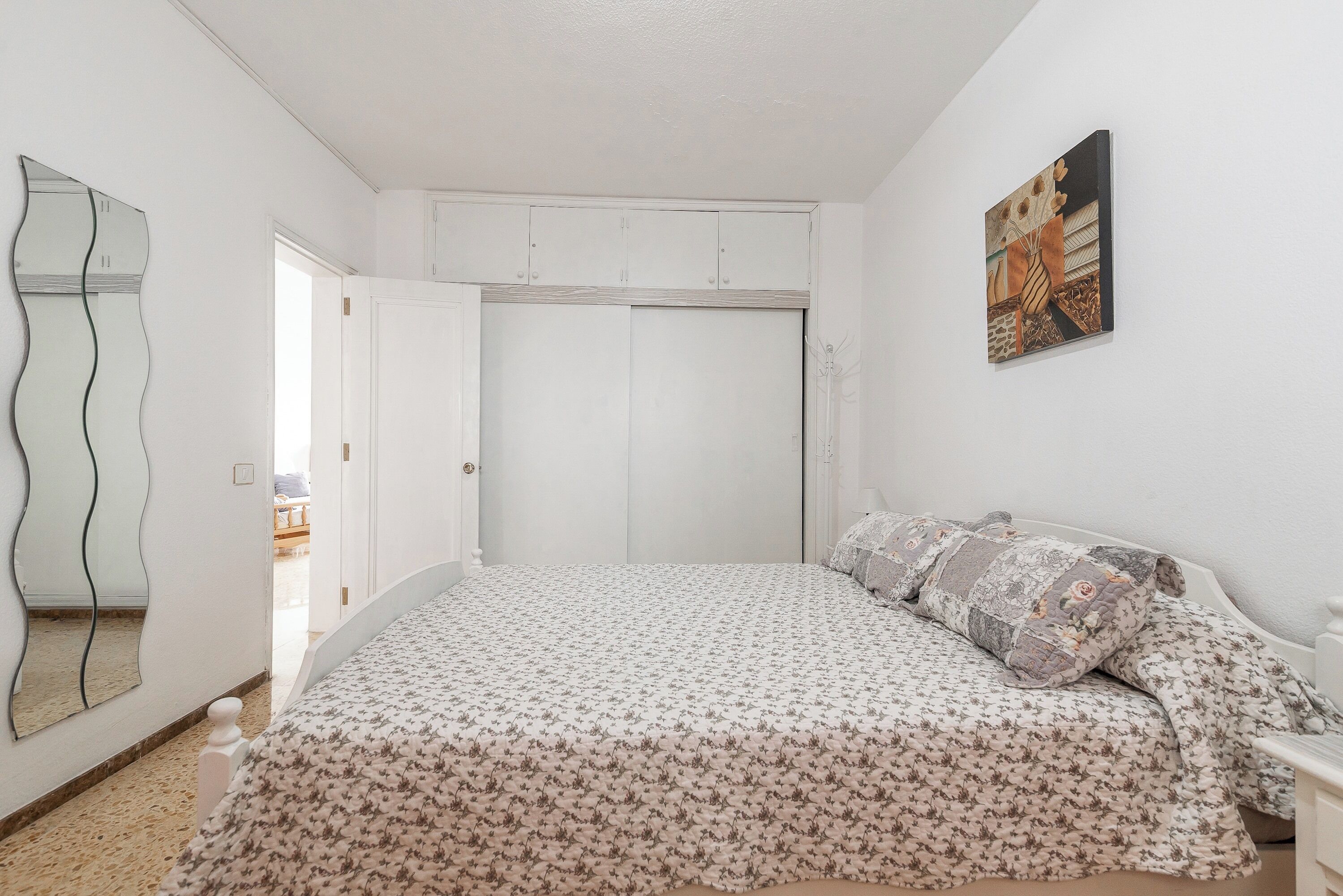 A bedroom with a bed, a wardrobe, a mirror, and a painting on the wall.