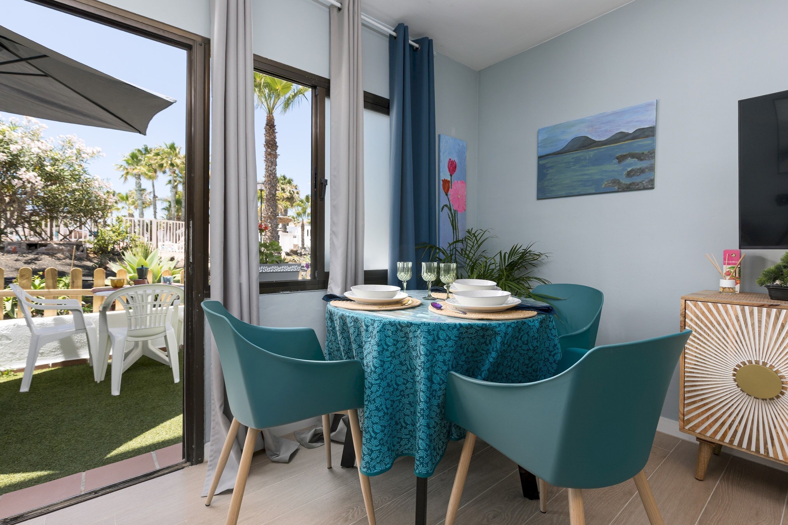 A dining area with a table set for four, chairs, a TV, and a painting on the wall.