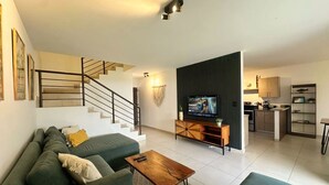 A modern living room with a staircase, a sofa, a coffee table, a TV, and a kitchen area. - Beautiful 5-BR House with AC in Zaragoza. Community Pool & Close to the Beach! (Zaragoza)
