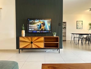 Un salon moderne avec un téléviseur à écran plat fixé à un meuble en bois, une table à manger et une plante en pot.