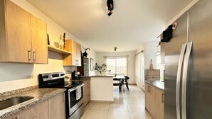 A modern kitchen with granite countertops, stainless steel appliances, wooden cabinets, and a central island with seating. - Beautiful 5-BR House with AC in Zaragoza. Community Pool & Close to the Beach! (Zaragoza)