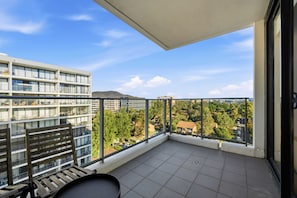 A balcony with a view of buildings and trees, a wooden chair, and a table. - Charming 2BR Apartment Near Canberra's Attractions (Canberra)