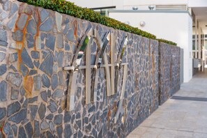 A stone wall with a geometric metal structure, a paved walkway, and a building in the background. - Charming 2BR Apartment Near Canberra's Attractions (Canberra)