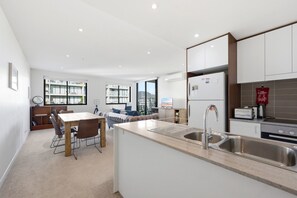A modern kitchen with a central island, a dining area with a table and chairs, and a view of the city through large windows. - Charming 2BR Apartment Near Canberra's Attractions (Canberra)