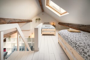A loft bedroom with a skylight, wooden beams, a bed with patterned bedding, a bench, and a small seating area. - 3-bedroom Apartment in National Residence (Antwerp)