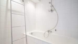 Um banheiro com azulejos brancos, banheira, chuveiro e porta-toalhas de metal.