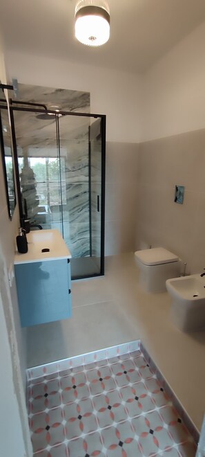 Un bagno moderno con box doccia in vetro, un water, un bidet e un lavabo con piano in marmo.