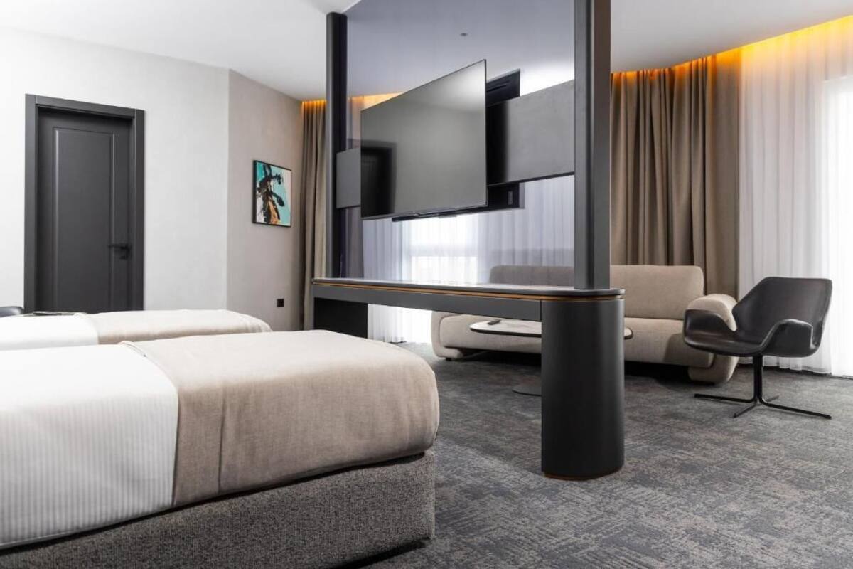Ein modernes Hotelzimmer mit zwei Betten, einem Flachbildfernseher, einer Couch und einem Sessel.