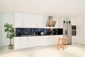 Una cocina moderna con armarios blancos, encimera negra, electrodomésticos de acero inoxidable y una planta en maceta.