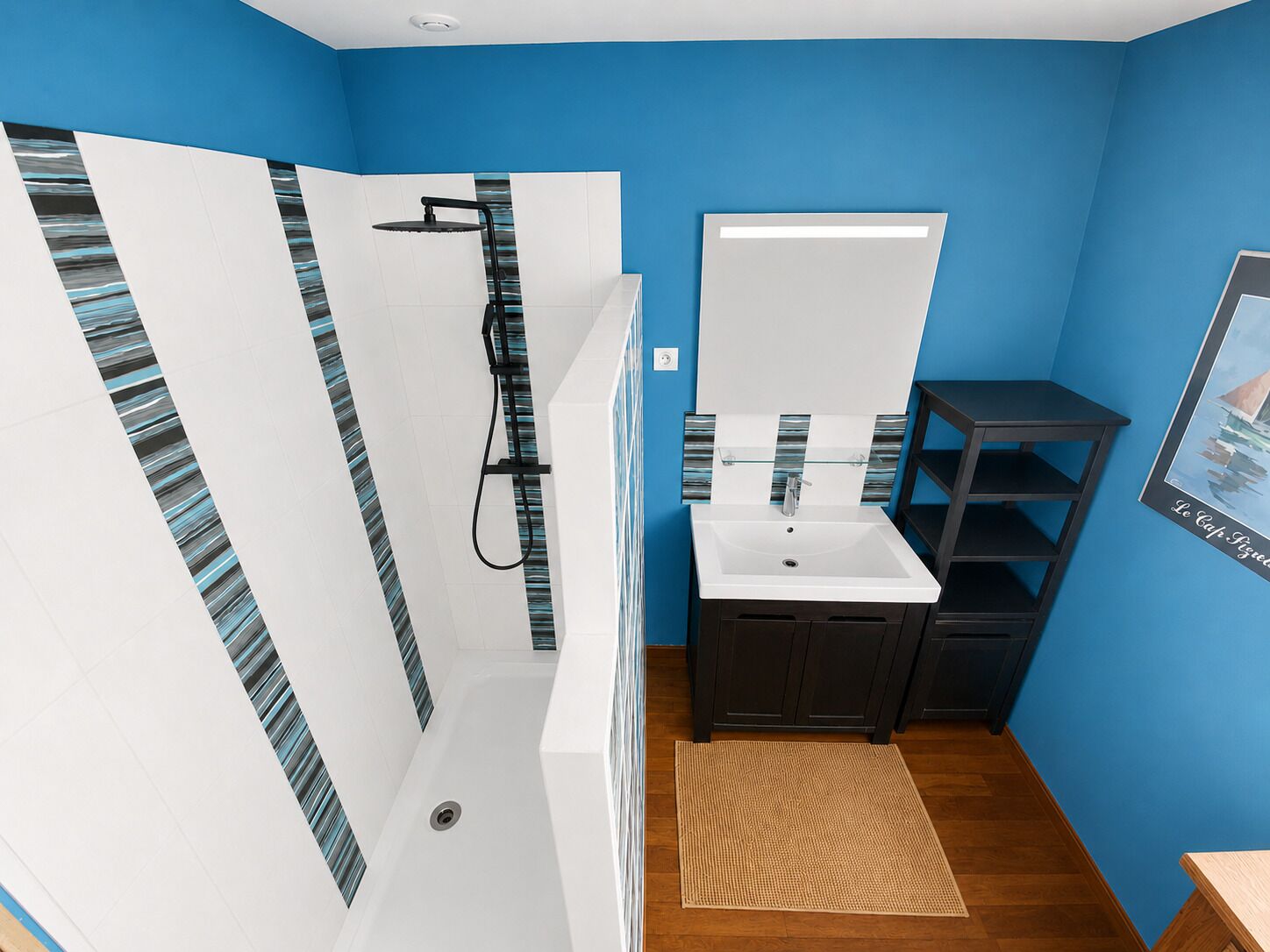 Une salle de bain avec une douche, un lavabo et des meubles sombres, le tout sur un fond de murs bleus.