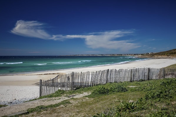 Ein Strand mit Holzlattenzaun, blauem Himmel und Wellen.