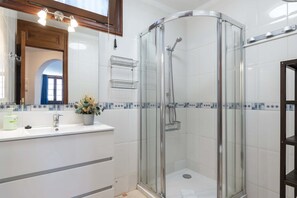 Ein modernes Badezimmer mit einer gläsernen Duschkabine, einem weißen Waschbecken mit Spiegel darüber und einer gefliesten Rückwand.