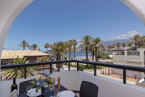 Ein Balkon mit Esstisch, der auf einen Strand mit Palmen und einem klaren Himmel blickt.