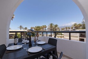 Ein Balkon mit Tisch für zwei Personen, Blick auf Palmen und einen klaren Himmel.