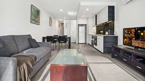 Una sala de estar moderna con un sofá, una mesa de centro y un televisor. Hay una zona de cocina con una barra y un comedor con sillas.