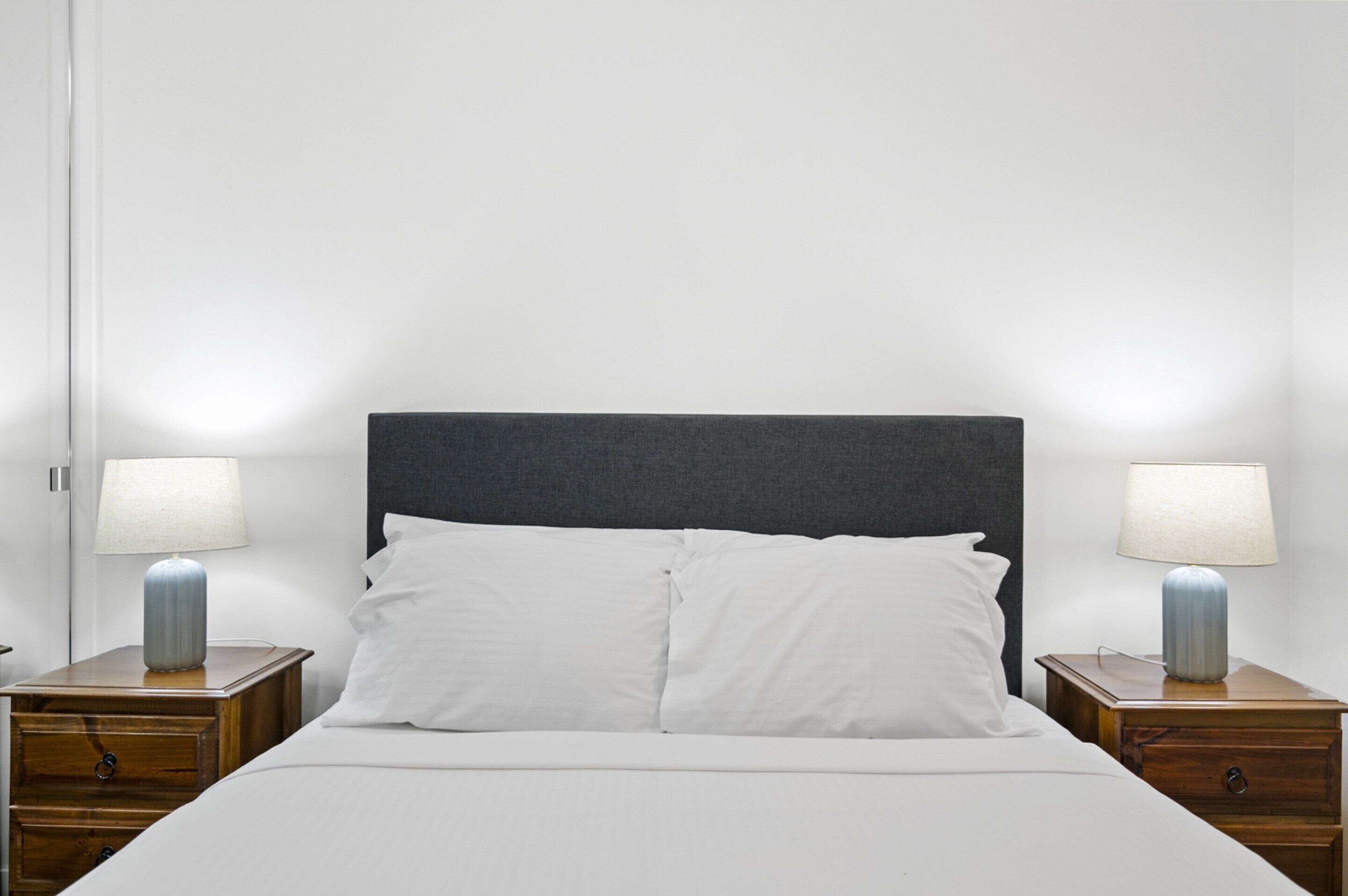 Un lit avec une literie blanche, une tête de lit sombre et deux tables de chevet avec des lampes.