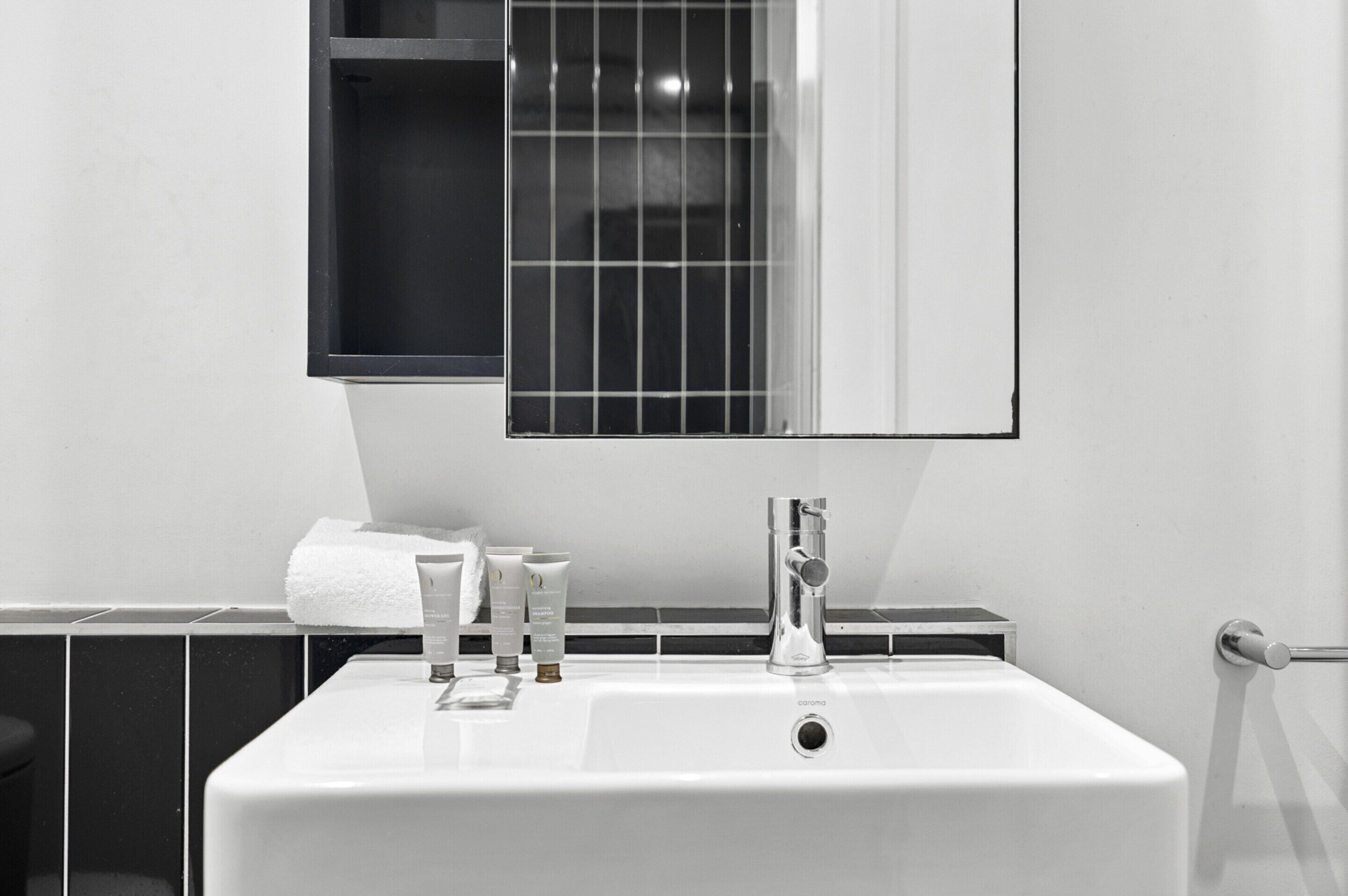Un baño con lavamanos blanco, espejo y artículos de aseo.