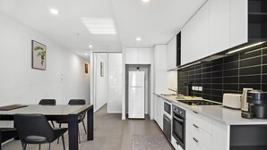Una cocina moderna con gabinetes blancos, salpicadero de baldosas negras, horno empotrado y un comedor con mesa y sillas.