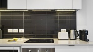 Una cocina moderna con salpicadero de azulejos negros, armarios blancos, estufa empotrada, tostadora, cafetera y microondas.