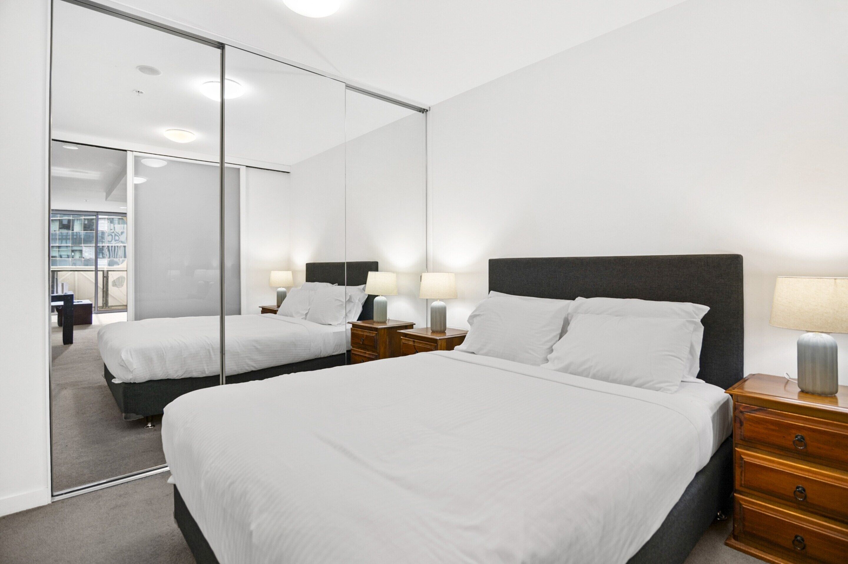 A hotel room with two beds, a large mirror, and a view of the cityscape.