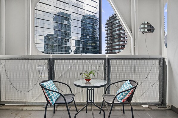 Un balcon avec deux chaises, une petite table et un pot de fleurs.
