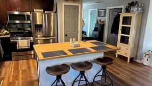 Una cocina moderna con electrodomésticos de acero inoxidable, una isla de madera con taburetes altos y un armario blanco con puertas de vidrio.