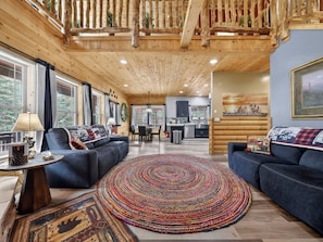 A log cabin interior with a dining area, kitchen, and two sofas with a colorful rug. - Treetop Lodge | 3 bdrm Duck Creek Cabin (Duck Creek Village)