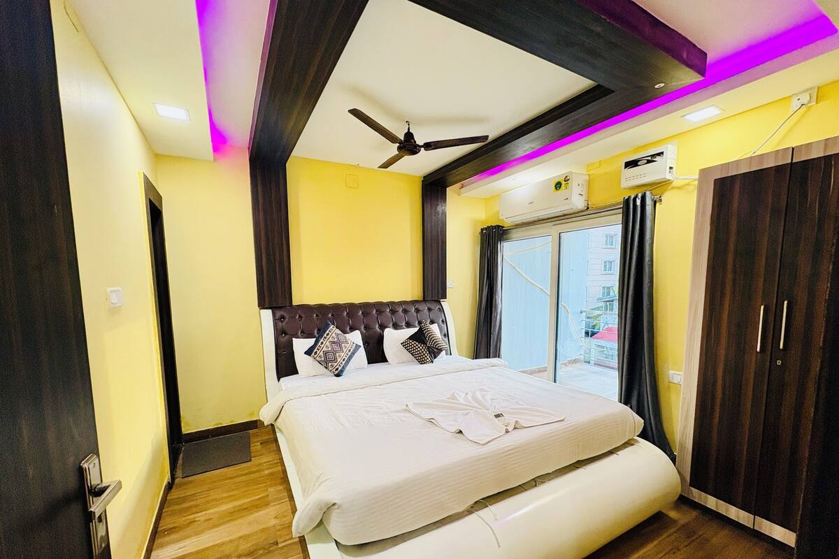 A bedroom with a bed, ceiling fan, air conditioning unit, and a view through a glass door.
