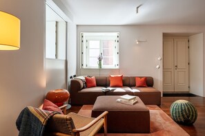 Ett modernt vardagsrum med en soffa, en pall och en fåtölj. Det finns ett fönster med utsikt, en dörr och en lampa.