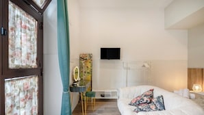 A hotel room with a bed, a vanity with a mirror, a television, and a large window with curtains.