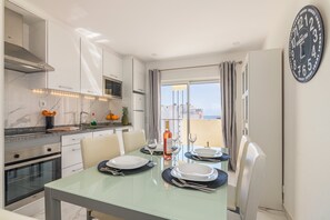 Una cuina moderna amb armaris blancs, una campana d'extracció d'acer inoxidable i una zona de dinar amb una taula de vidre per a quatre persones.