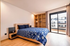 A modern bedroom with a bed, wooden headboard, built-in shelving, and a large window with a view of buildings. - La Maison N°17 - An exceptional haven of peace (Rabat)