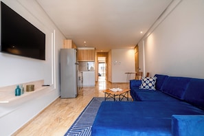 A modern living room with a blue sofa, a flat-screen TV, and a kitchen area in the background. - La Maison N°17 - An exceptional haven of peace (Rabat)