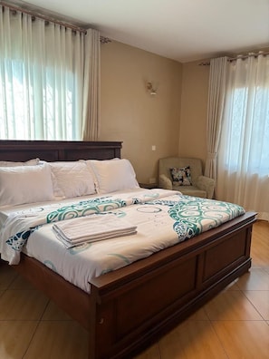 Quarto com uma cama grande, uma cadeira e cortinas.