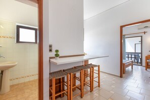A modern kitchen with a white countertop, wooden stools, and a small potted plant. - Apartment 'Popi 2-Bedroom' with Mountain View, Wi-Fi and Air Conditioning (Agia Marina)