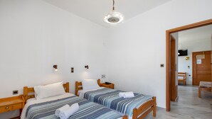 Un dormitorio con dos camas individuales, cabeceros de madera, mesitas de noche, una lámpara colgante y una puerta de madera que da a otra habitación.