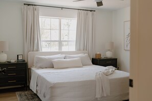 Ein Schlafzimmer mit Bett, Vorhängen, einem Nachttisch, einer Lampe und einem Wandbild.