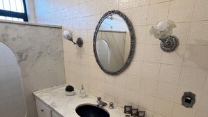 Ein Badezimmer mit Marmorwaschbecken, einem runden Spiegel mit aufwendigem Rahmen und einer Toilette.
