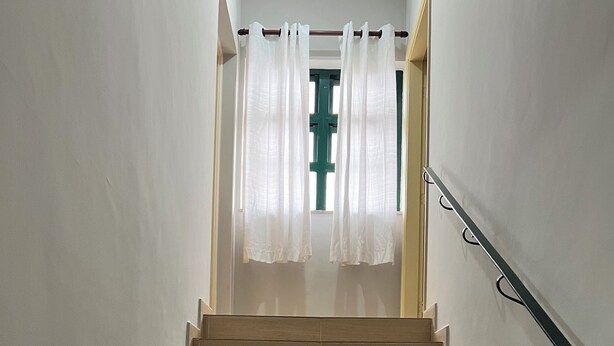 Eine Treppe mit Handlauf, weißen Wänden und einem Fenster mit Vorhängen.