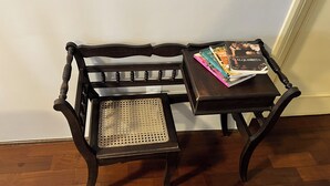 Ein Holzstuhl mit gewobener Sitzfläche und Lehne, platziert neben einem kleinen Tisch mit einem Buch mit dem Titel 'Contigo Alquimista' und weiteren Büchern.