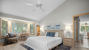 Une chambre à coucher avec un grand lit, un bureau, une chaise, un ventilateur de plafond et une vue sur l’extérieur.