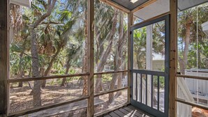 Une véranda couverte avec des balustrades en bois, une vue sur les arbres et une clôture blanche en arrière-plan.