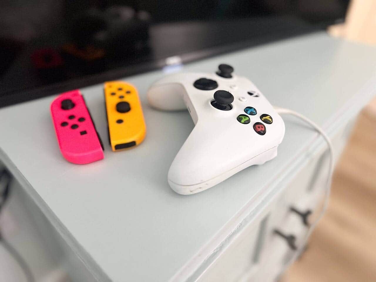 A white gaming controller on a light-colored surface with two colorful controllers beside it.