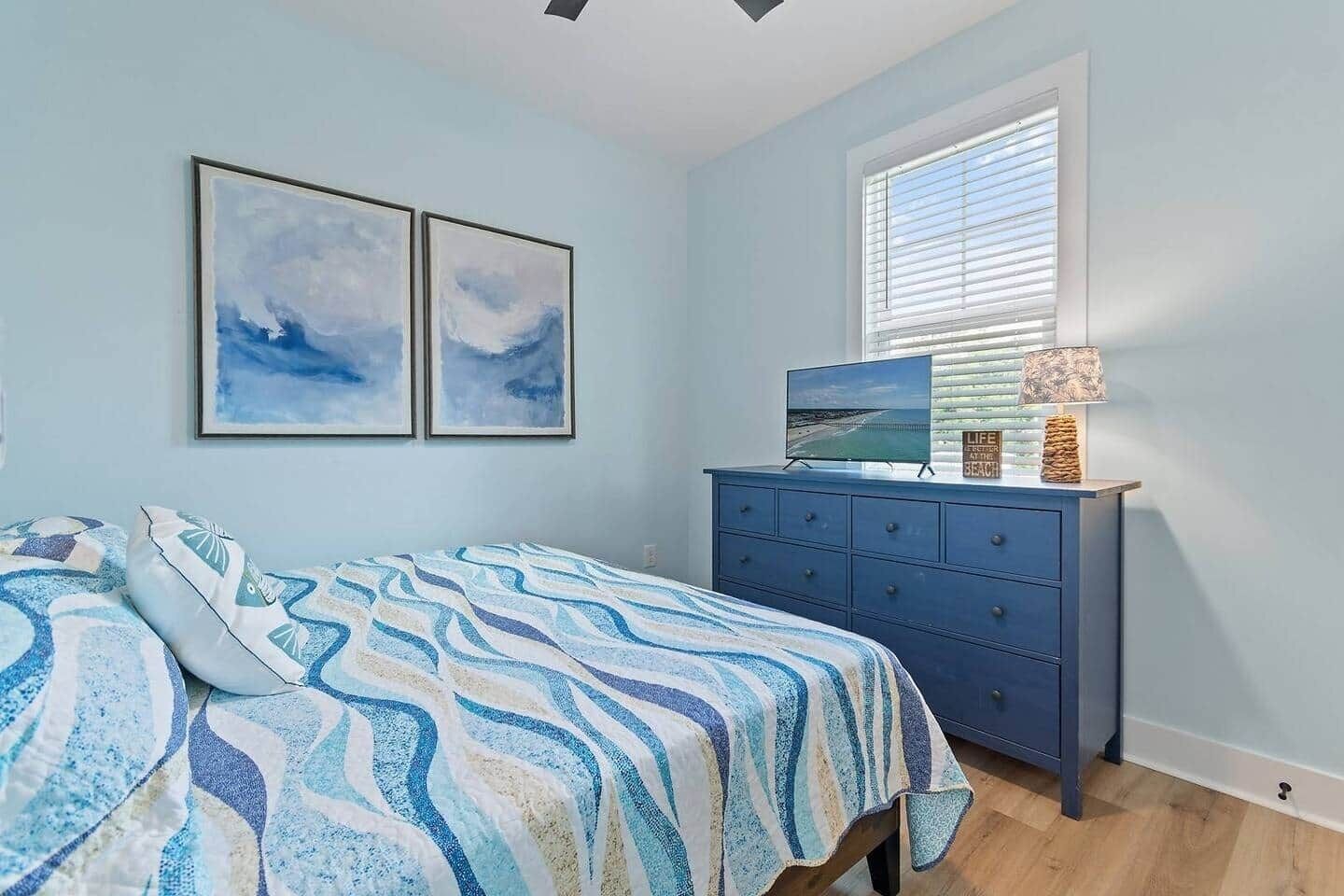 A bedroom with a bed, a dresser, a TV, and two wall-mounted pictures.