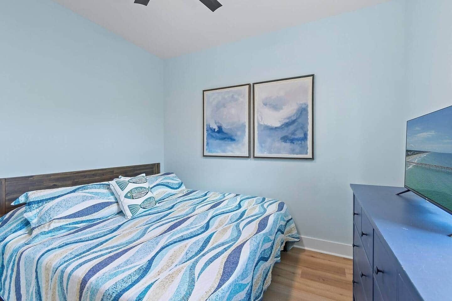 Ein Schlafzimmer mit einem Bett, einem Schminktisch und zwei gerahmten Kunstwerken an der Wand.