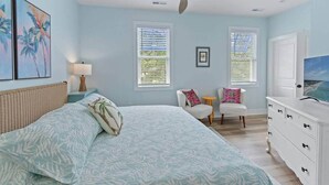Une chambre à coucher avec un lit, deux chaises, un téléviseur et un ventilateur de plafond.