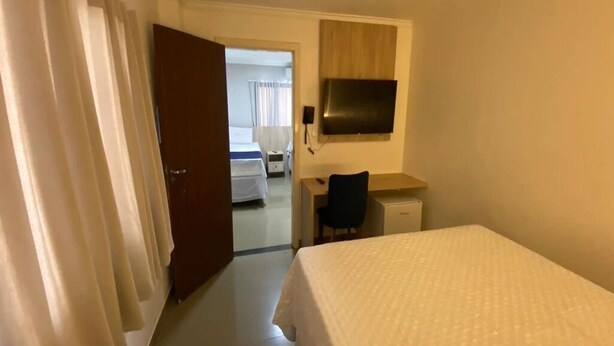 Une chambre d’hôtel équipée d’un lit, d’un bureau, d’une chaise, d’une télévision et d’une porte donnant sur une autre pièce.