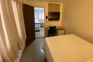 A hotel room with a bed, a desk, a chair, a television, and a door leading to another room. - Hotel Bastos (Euclides Da Cunha)